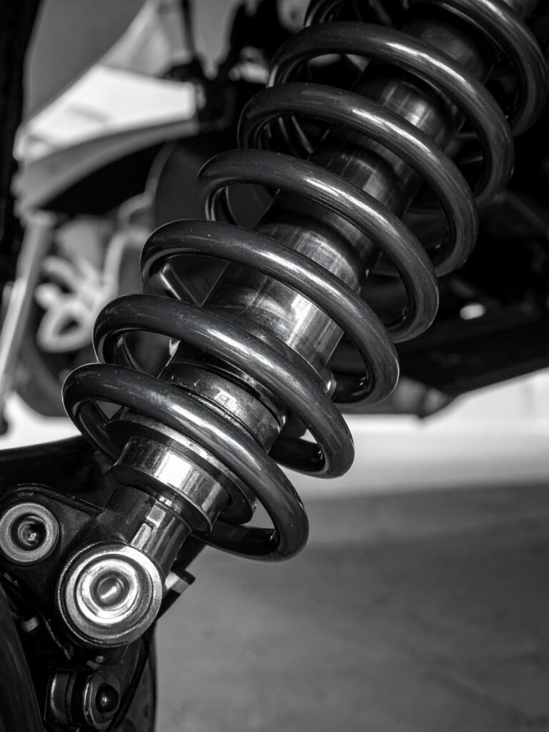 Close-up black and white view of a vehicle's suspension shock absorber and coil spring.